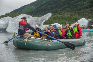 Group of happy travelers in raft kayaking in summer Alaska fjords glaciers icebergs
